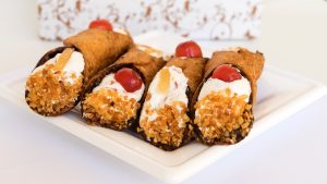 Cannoli siciliani artigianali con crema di ricotta e canditi su piatto bianco.